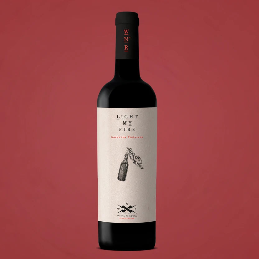 A bottle of wines and roses Light My Fire Garnache Tinto red wine, featuring a cream-colored label with black text and illustration, and a black neck sleeve with red lettering.