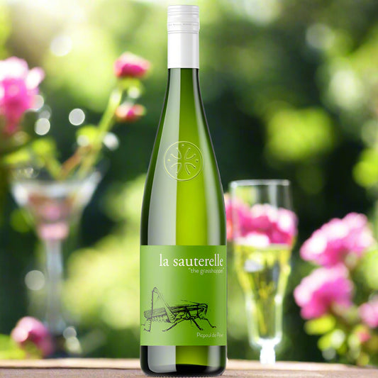 Green bottle of white wine with a picture of a grasshopper on the label. Its sat in a garden surrounded by pink flowers 
