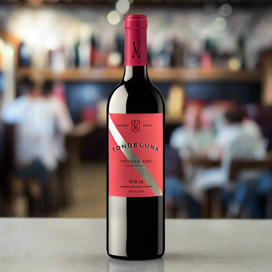 bottle of tondeluna crianza which is a red wine. it has a red label with a silver band diagonally across the label. it's on a bar in a restaurant